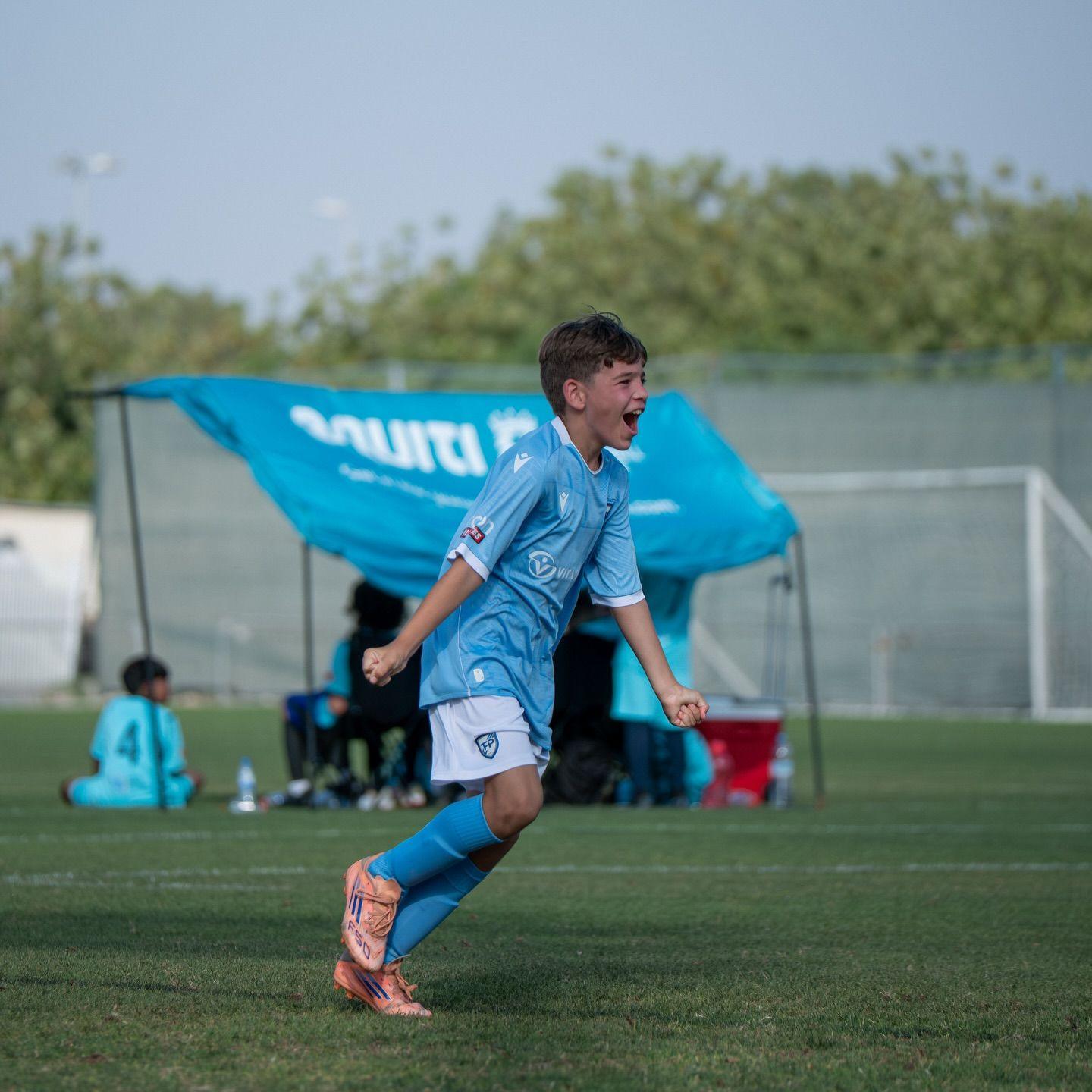 An EYFL player celebrates a goal in front of the Equiti team tent